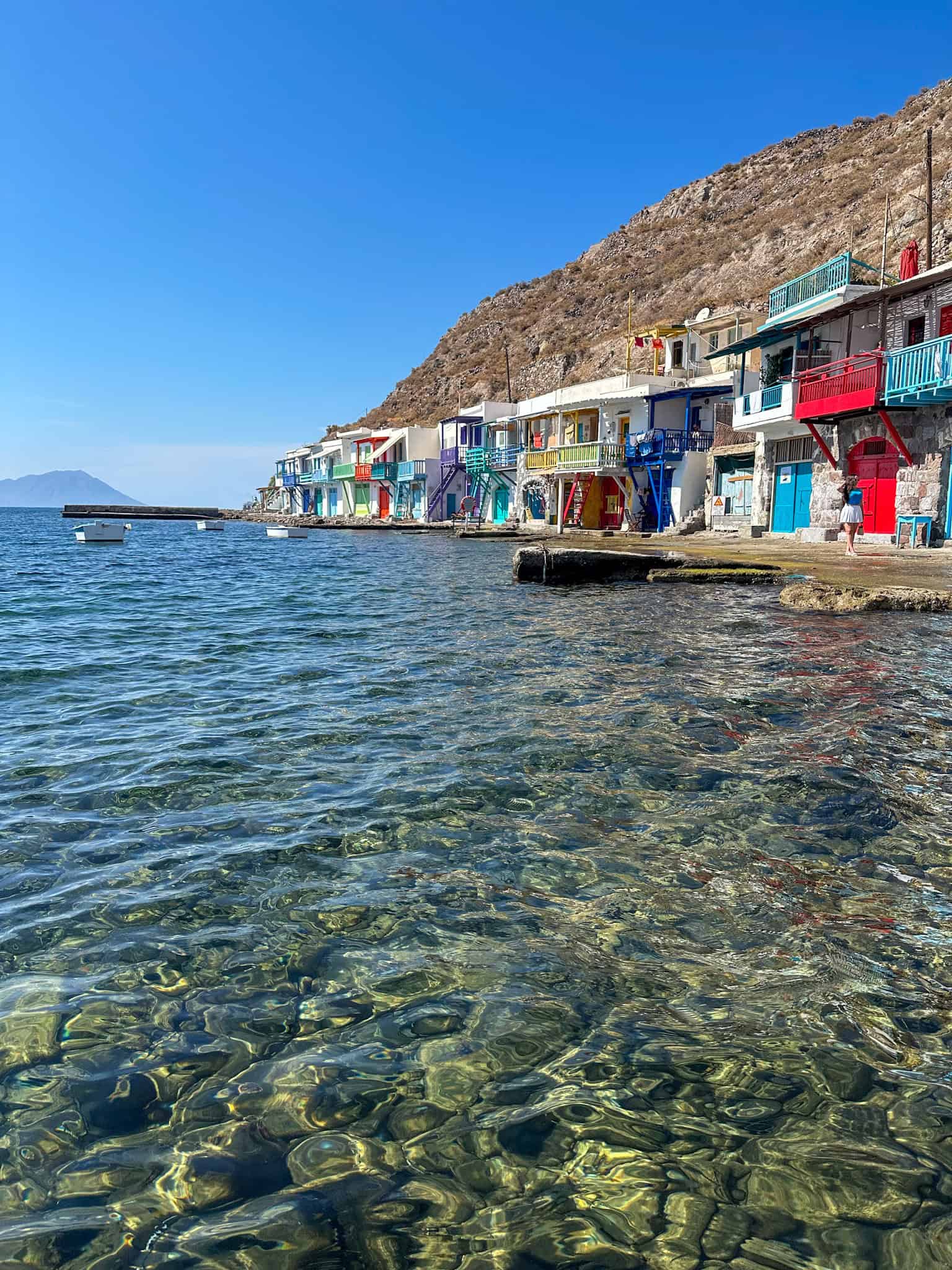 A row of traditional boathouses on the water's edge, each with a different brightly colored door.
