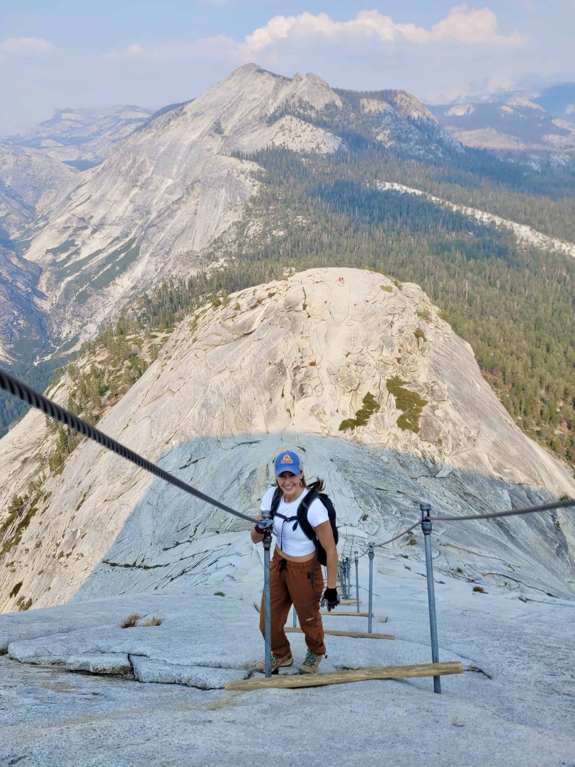 Kait smiling while climbing the Half Dome cables in Yosemite with granite peaks in the background.