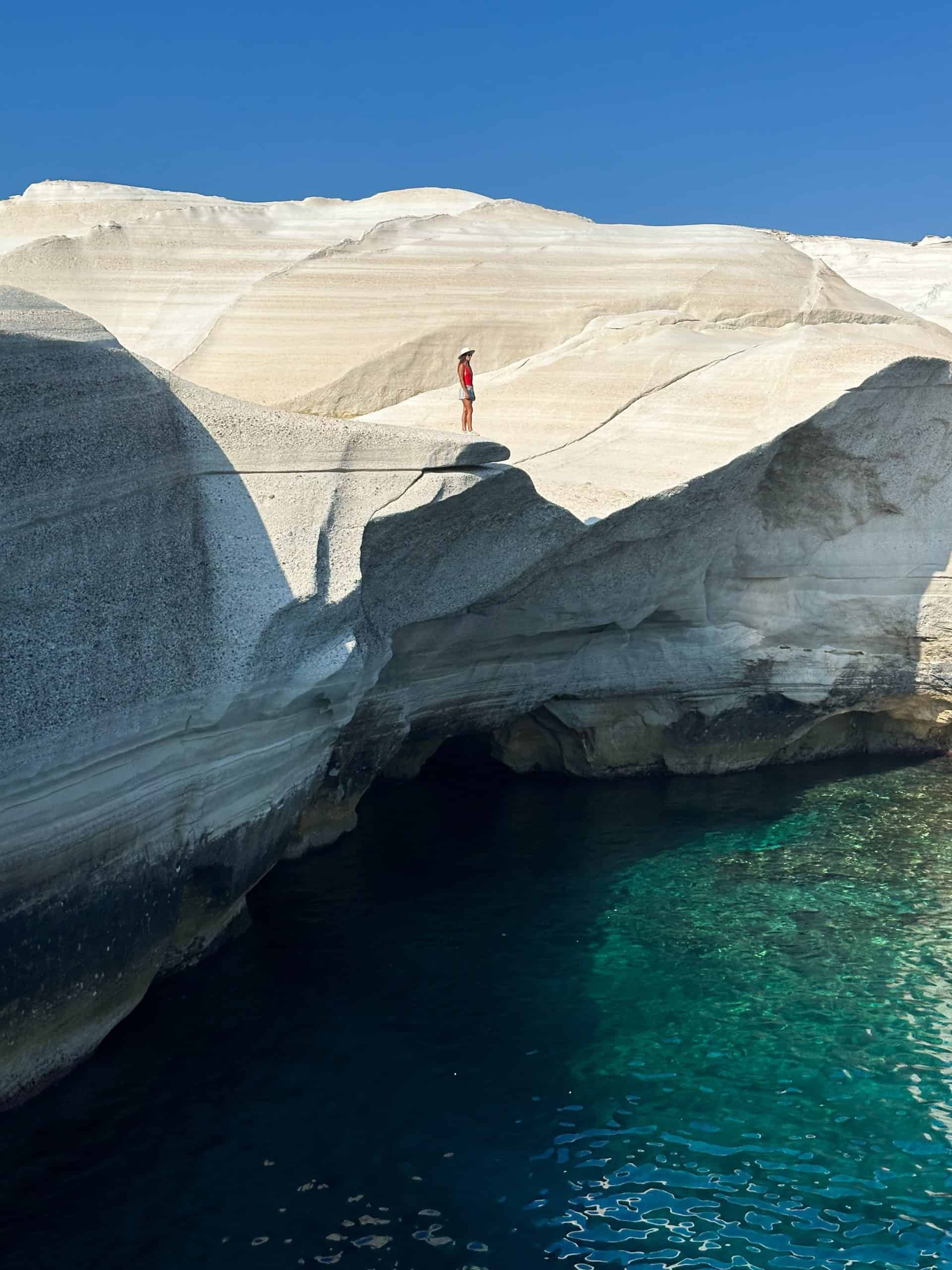 Kait standing on the white volcanic rock formations at Sarakiniko Beach in Milos, overlooking the turquoise Aegean Sea.
